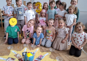grupa dzieci, w środku siedzi dziewczynka z różową koroną i balonem