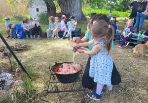 Zdjęcie przedstawia dziewczynkę wsypującą przyprawę do kociołka.