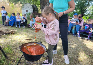Zdjęcie przedstawia dziewczynkę wlewającą sos do kociołka.