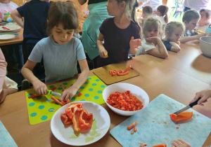 Zdjęcie przedstawia dziewczynkę krojącą paprykę.