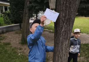 Na zdjęciu widzimy chłopca, który odnalazł powieszoną zagadkę w ogrodzie przedszkolnym.