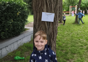 Na zdjęciu widzimy chłopca, który odnalazł powieszoną zagadkę w ogrodzie przedszkolnym.