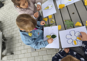 Na zdjęciu widzimy dzieci, które przyklejają materiał naturalny na szablony.