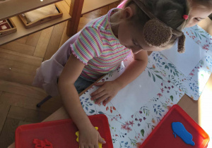 Na zdjęciu widzimy dziewczynkę, która odciska dłoń w żółtej farbie.