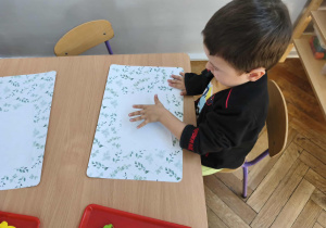 Na zdjęciu widzimy chłopca, który odciska dloń zamoczoną w farbie na kartkę papieru.