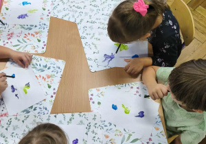 Na zdjęciu widzimy grupkę dzieci, które rozdmuchują plamy z wykorzystaniem rurki.