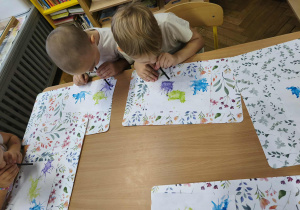 Na zdjęciu widzimy dwóch chlopców, którzy rozdumuchą kolorowe kleksy z farby za pomocą dmuchania w rurkę.