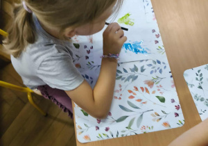 Na zdjęciu widzimy dziewczynkę, która rozdmuchuje plamy farby za pomocą rurki.