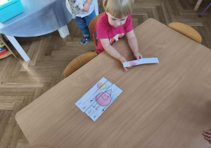 Na zdjęciu widzimy dziewczynkę, która próbuje ułożyć puzzle z kropką.