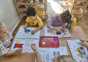 Na zdjęciu widzimy dzieci, które tworzą pracę plastyczną z wykorzystaniem stempli w kształcie kropki.