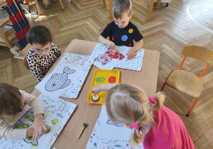 Na zdjęciu widzimy dzieci, które tworzą pracę plastyczną z wykorzystaniem stempli w kształcie kropki.