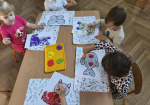 Na zdjęciu widzimy dzieci, które tworzą pracę plastyczną z wykorzystaniem stempli w kształcie kropki.