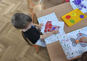 Na zdjęciu widzimy chłopca, który z wykorzystaniem stempla w kształcie kropki wykonuje prace plastyczną.