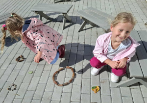 dziewczynki układją kropki z naturalnego materiału zebranegow ogródzie przedszkolnym