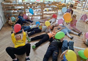 dzieci leżą na podłodze dmuchając w balon