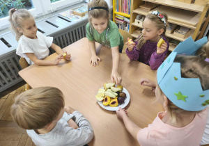 Na zdjęciu widzimy dziewczynkę, która częstuje dzieci owocami.