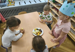 Na zdjęciu widzimy dziewczynkę, która częstuje dzieci owocami.