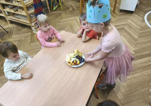 Na zdjęciu widzimy dziewczynkę, która częstuje dzieci owocami.