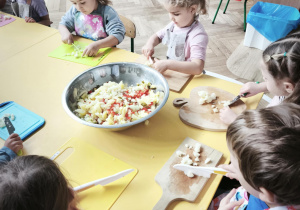 Dzieci wkładają pokrojone produkty do wspólnej miski