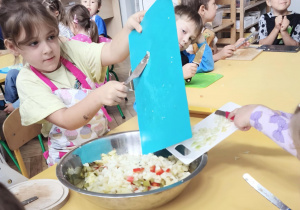 Dzieci wkładają pokrojone produkty do wspólnej miski