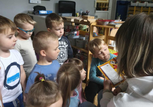 Na zdjęciu widzimy grupkę dzieci, które słuchają i oglądają ilustracje.
