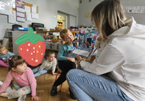 Na zdjęciu widzimy grupkę dzieci, które słuchają i oglądają ilustracje.