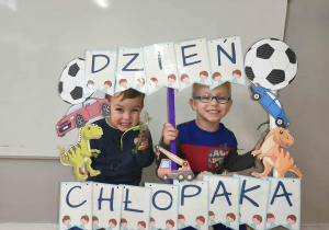 Na zdjęciu widzimy dwójkę chłopców, którzy trzymają fotobudkę z napisem "Dzień Chłopaka".