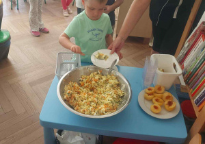 Zdjęcie przedstawia chłopca wkładającego sobie sałatkę na talerz.