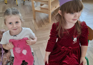 dwie dziewczynki, jedna siedzi na krześle, druga klęczy, trzyma w rękach śpiochy