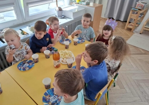 dzieci siedzą przy stole urodzinowym i jedzą
