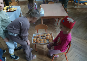 Na zdjęciu widzimy dziewczynkę, która częstuje dzieci babeczkami.