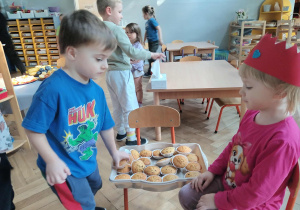 Na zdjęciu widzimy dziewczynkę, która częstuje dzieci babeczkami.