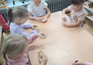 Dzieci siedzą przy stoliku i robią jeże z ziemniaków.