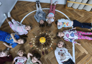 Dzieci leżą na podłodze wokół ułożonej madali z darów natury.