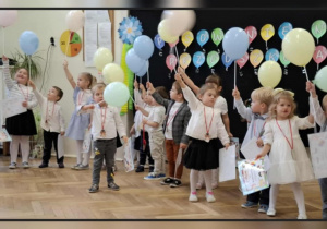 Dzieci stojące po pasowaniu z balonami, dyplomami i medalami