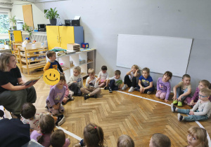 Na zdjęciu widzimy grupkę dzieci, które słuchają wierszy czytanych przez mamę Poli.