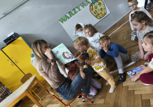 Na zdjęciu widzimy grupkę dzieci, które słuchają czytanej opowieści.