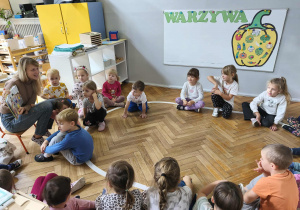 Na zdjęciu widzimy grupkę dzieci, które słuchają czytanej opowieści oraz oglądają ilustrację w książce.