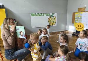 Na zdjęciu widzimy grupkę dzieci, które słuchają czytanej opowieści oraz oglądają ilustrację w książce.