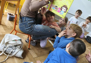 Na zdjęciu widzimy grupkę dzieci, które słuchają czytanej opowieści oraz oglądają ilustrację w książce.