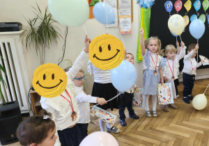 Na zdjęciu widzimy grupkę dzieci, które zostały Pasowane na Przedszkolaka. Dzieci na szyjach mają zawieszone medale z misiem, w ręku trzymają balony i dyplom.