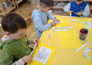 chłopcy wycinają i przyklejają na kartkę wycięte z papieru liście