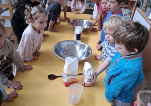 dzieci stoją przy stolikach na których znajdują się materiały do przygotowania masy solnej