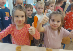 Na zdjęciu dwie dziewczynki, które pokazują kciuki do góry na znak smacznego wykonanego musu