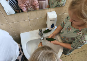 Na zdjęciu widzimy dwie dziewczynki, które myją pod bierzącą wodą marchewkę i ogórka.