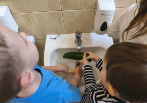 Na zdjęciu widzimy chłopców, którzy myją pod bierzącą wodą pietruszkę i cukinię.