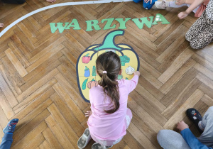 Na zdjęciu widzimy dziewczynkę, która dopasowuje warzywo do jego cienia na wielkiej papryce.