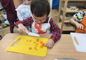 Na zdjęciu widzimy dziewczynkę, która kroi nożem marchewkę do sałatki jarzynowej.