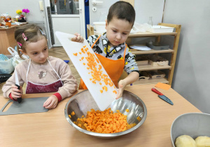 Na zdjęciu widzimy chłopca, który zsuwa do miski pokrojoną marchewkę.