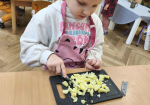 Na zdjęciu widzimy dziewczynkę, która kroi nożem ziemniaka.